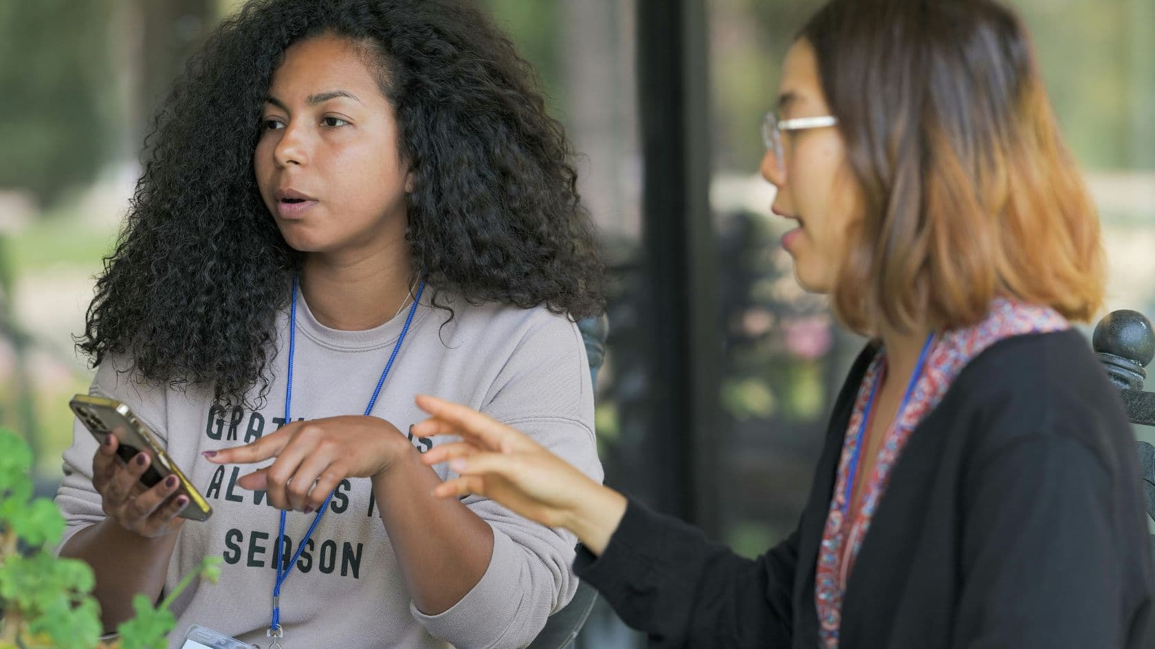 Close-up of hands holding a phone while a second person gestures toward the screen in conversation.